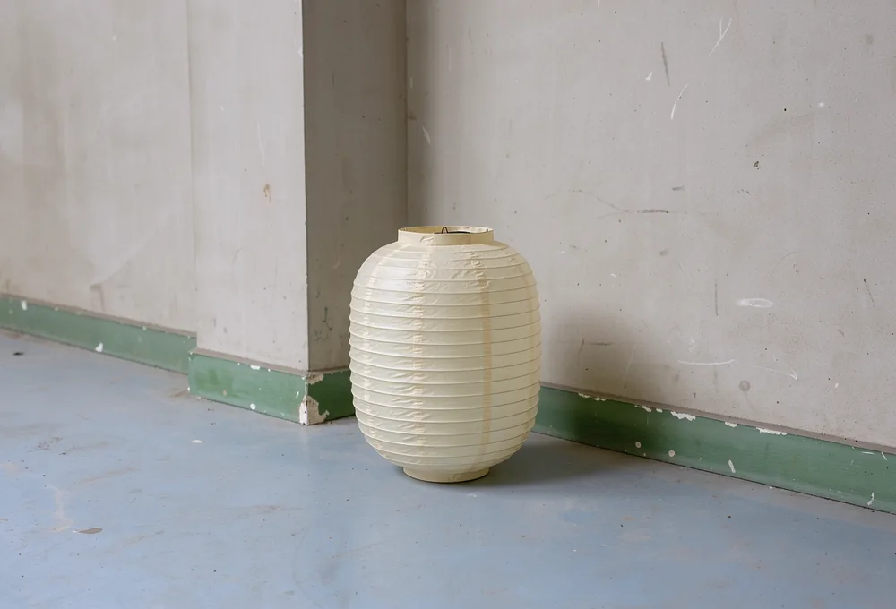 A cream paper lantern resting beside a pale veranda corner