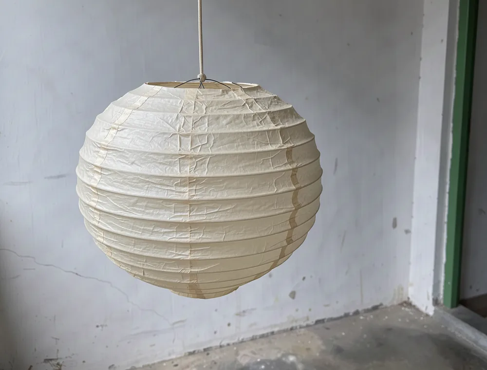 A cream lantern and its paper seams beside a cool white veranda wall